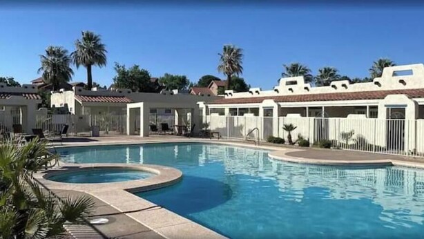 Une piscine avec un jacuzzi, entourée de palmiers et d’une clôture blanche.