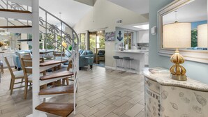 A spacious living area with a wooden staircase, a dining area with light blue chairs, and a kitchen with a large mirror and a decorative lamp. - Great Cottage at Hidden Dunes with Free Seasonal Beach Chair Setup! (Miramar Beach)