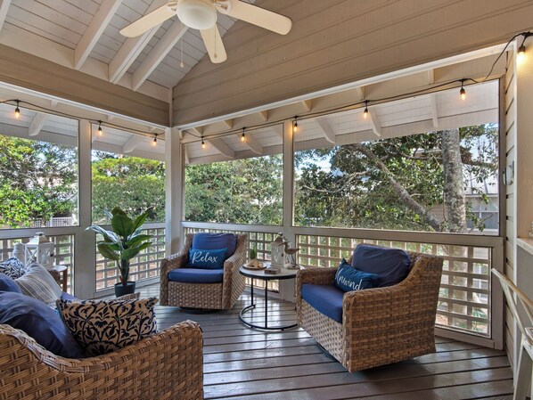 A covered porch with wicker furniture, a ceiling fan, and string lights.