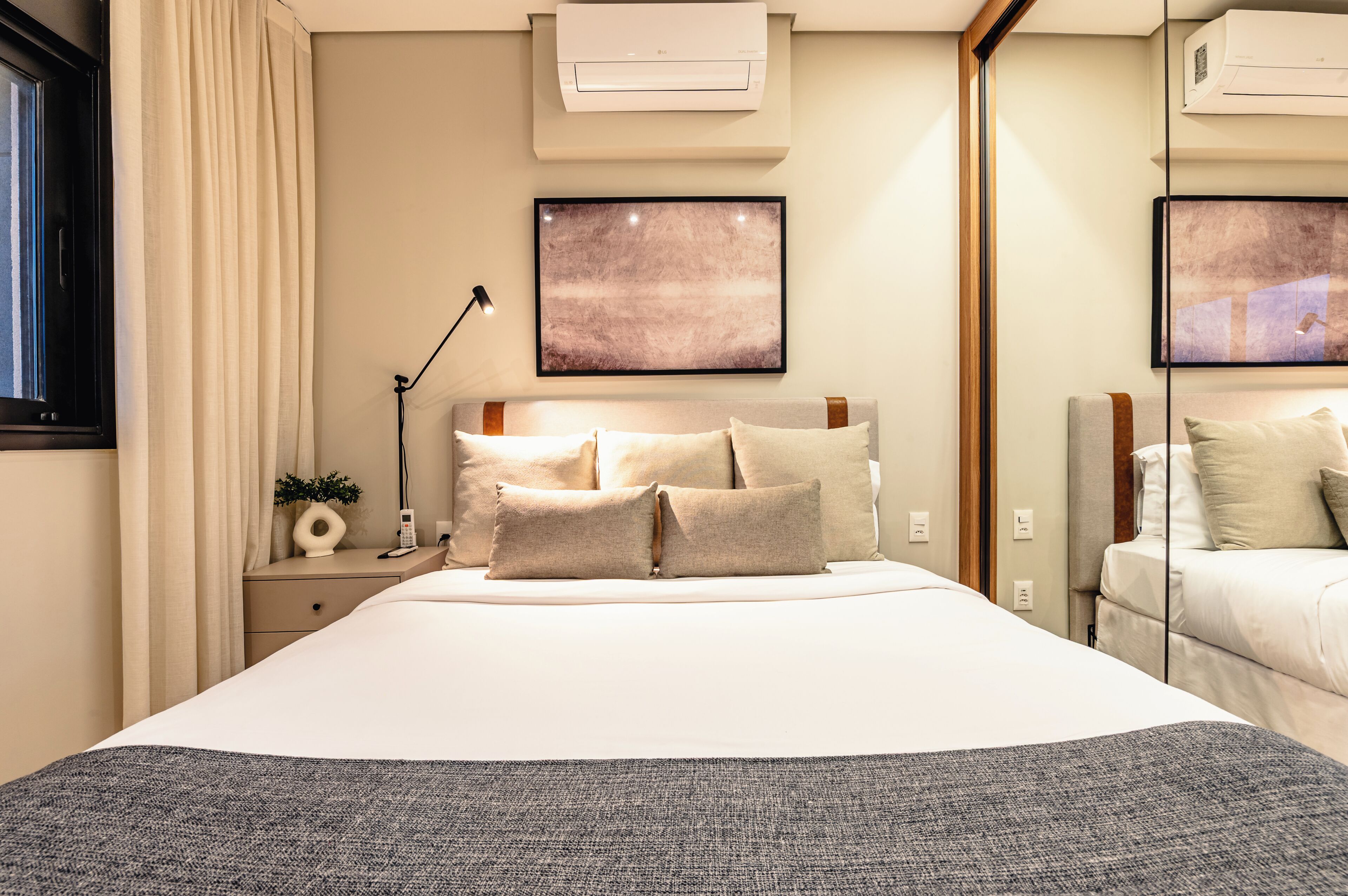 A neatly arranged bedroom with a large bed, bedside tables, a lamp, and artwork on the walls.