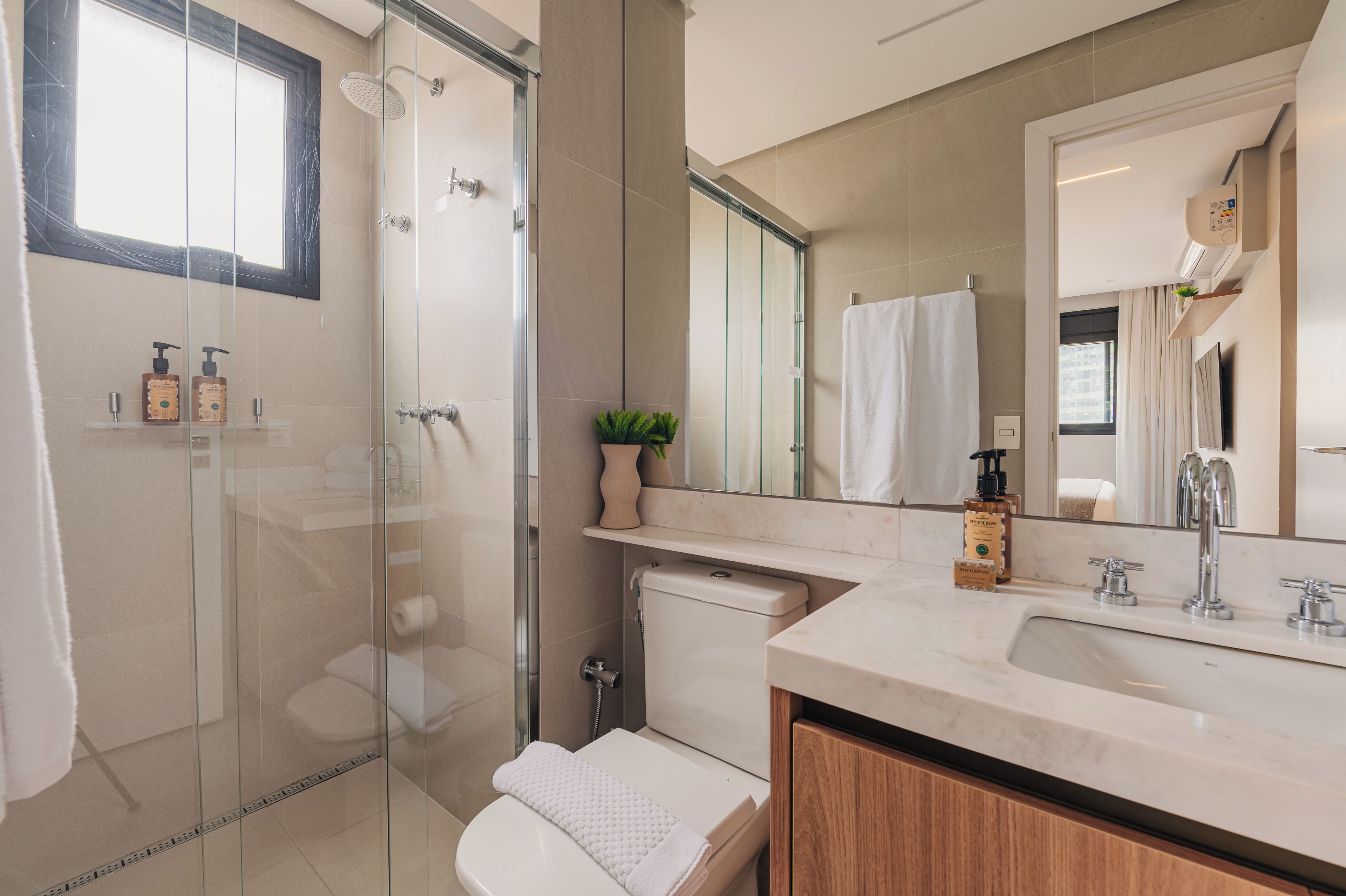 A modern bathroom with a glass-enclosed shower, a toilet, a sink with a mirror, and toiletries on the counter.