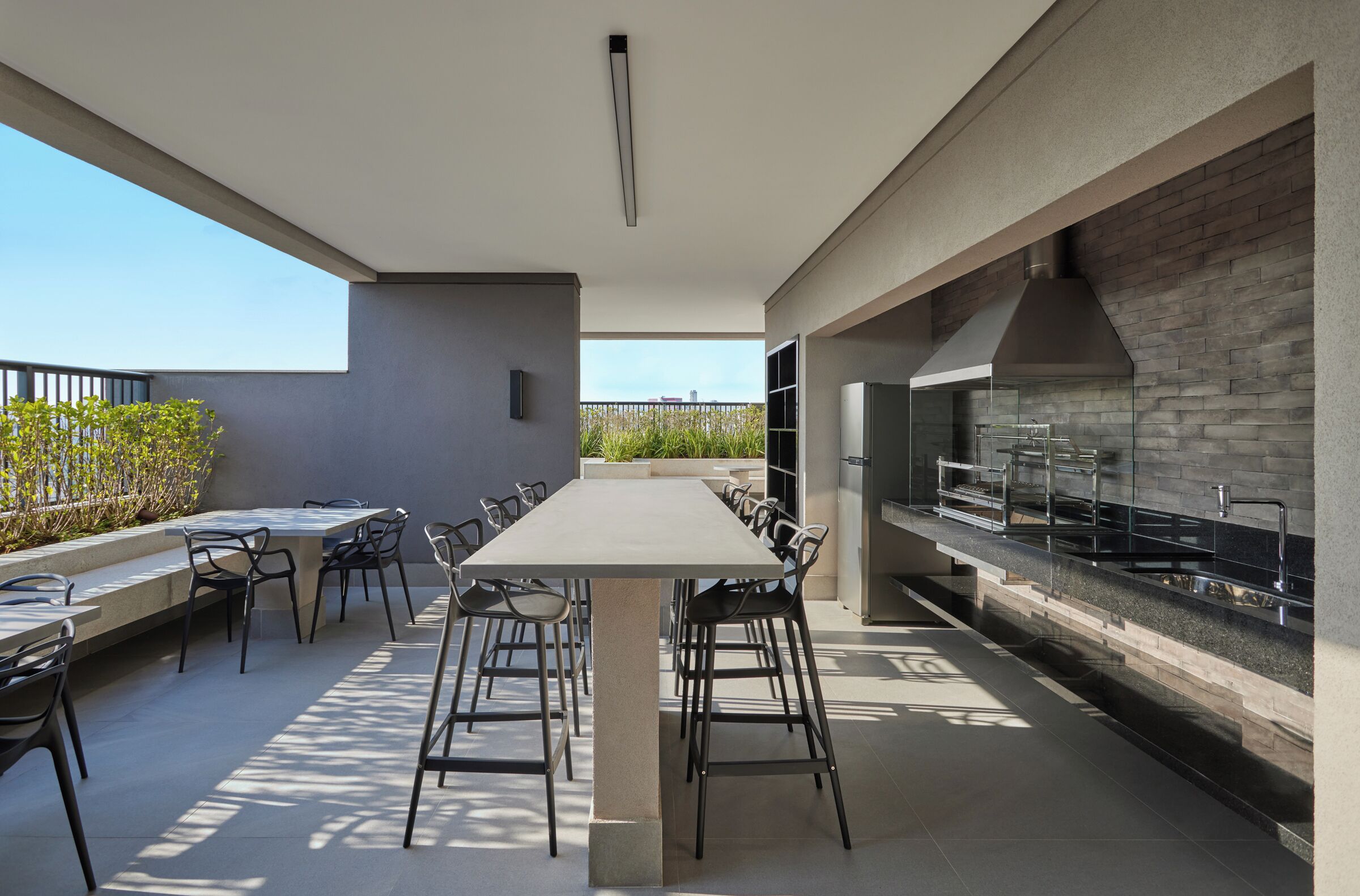 An outdoor dining area with a long table and chairs, a modern kitchen with a brick backsplash, and a view of the sky.