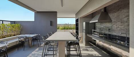 An outdoor dining area with a long table and chairs, a modern kitchen with a brick backsplash, and a view of the sky.