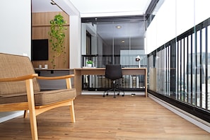 A modern office space with a wooden desk, a black office chair, a brown sofa, and a large window with a city view. - Movinn Expand - Pinheiros (São Paulo)