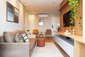 A modern living room with a sofa, chairs, a small table, and a kitchen area with a counter. - Movinn Expand - Pinheiros (São Paulo)