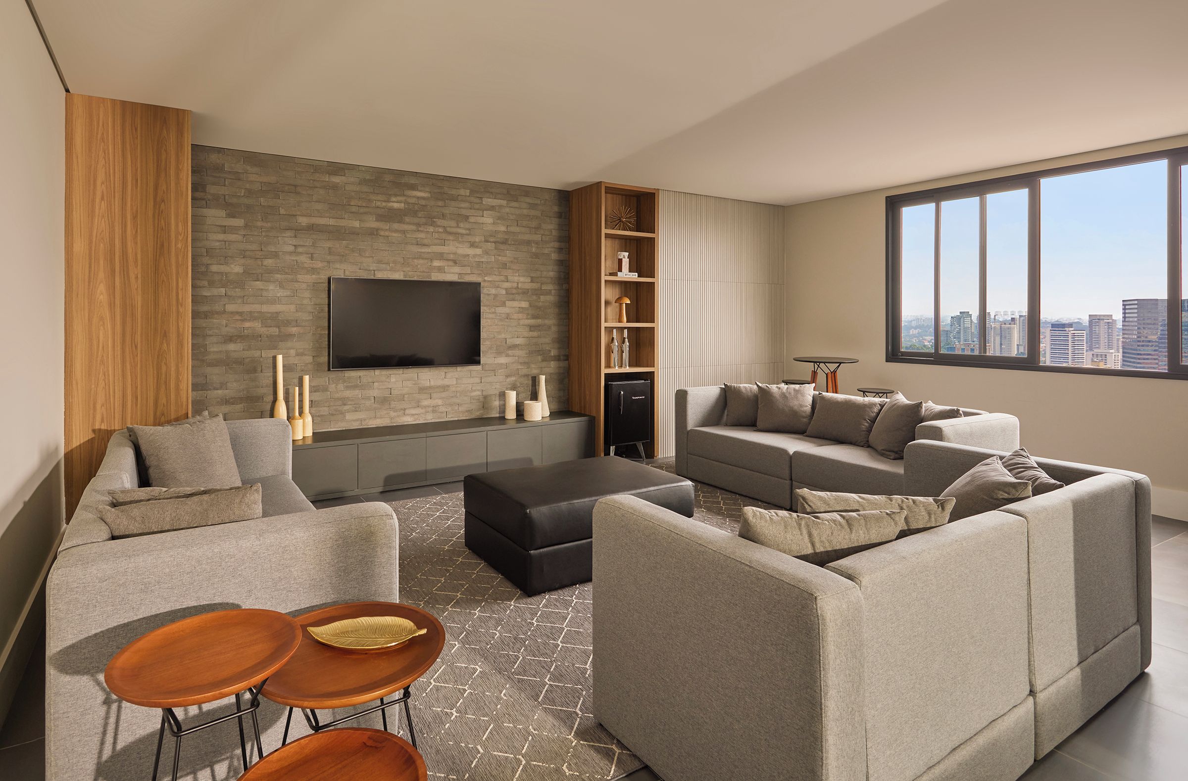 A modern living room with a flat-screen TV, grey sofas, a coffee table, and a bookshelf.
