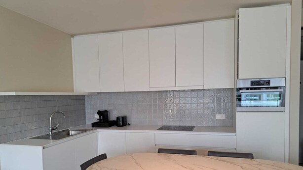 A compact kitchen with white cabinets, a marble countertop, a sink, a coffee maker, and an oven.