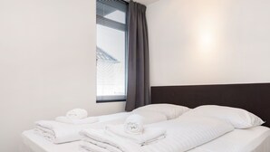 Una habitación de hotel con una cama bien hecha, una ventana con persianas y un cabecero oscuro.