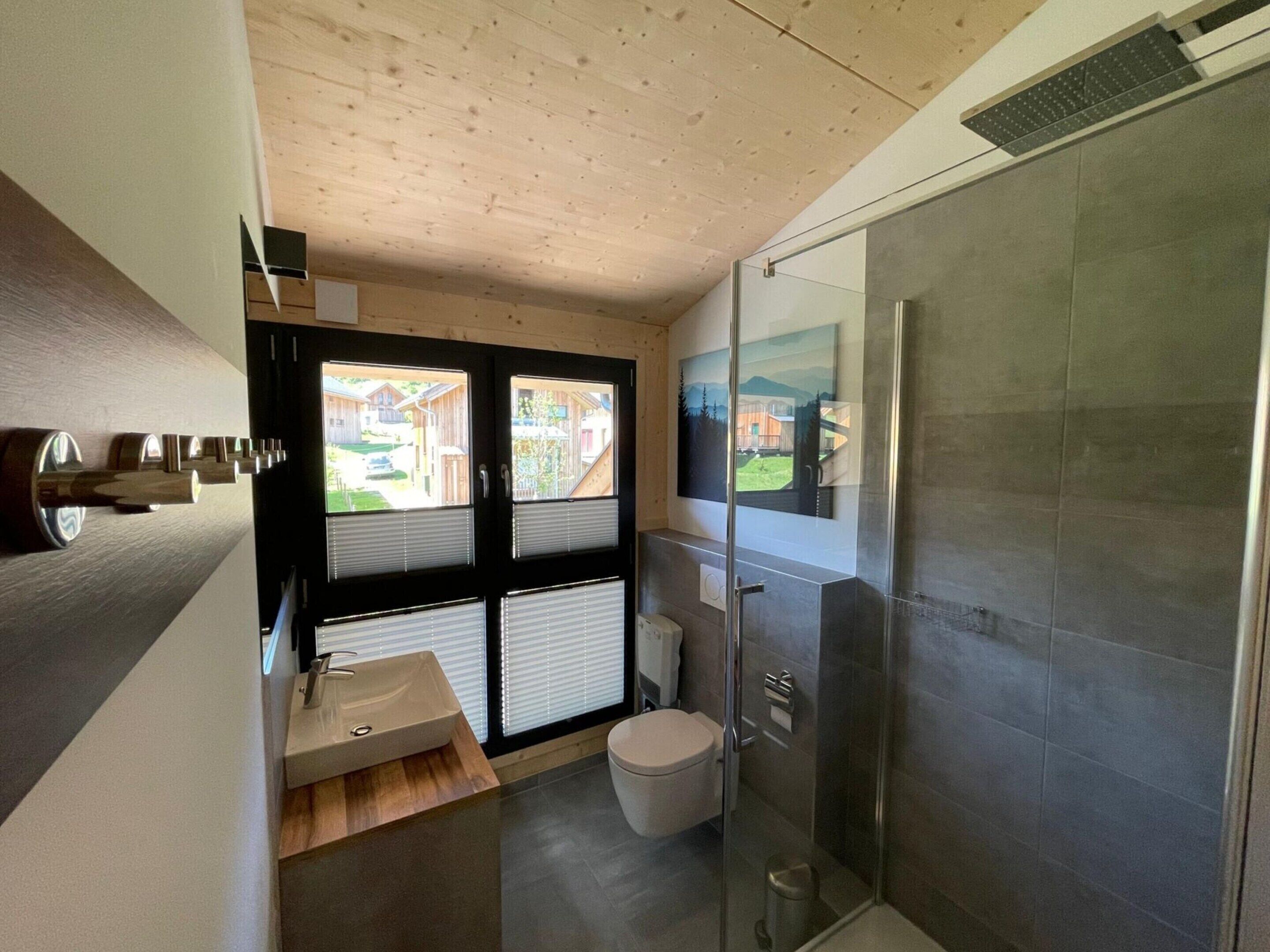 Et moderne badeværelse med træloft, brusekabine i glas, vask med træbordplade og toilet.