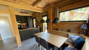 A modern kitchen with wooden beams, a dining area with a large table and chairs, and a cozy seating area with a sofa and cushions. - Attractive Chalet With Sauna (Sankt Georgen am Kreischberg)