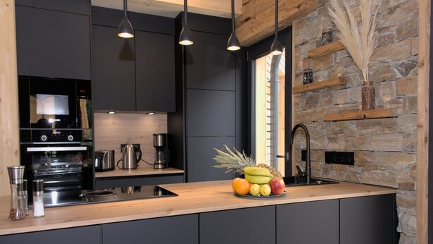 A modern kitchen with dark cabinetry, a wooden countertop, and a stone accent wall. - Attractive Chalet With Sauna (Sankt Georgen am Kreischberg)