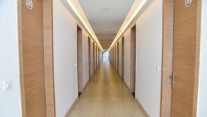 Un long couloir étroit d’hôtel, avec des portes en bois de chaque côté et un plancher de couleur claire.