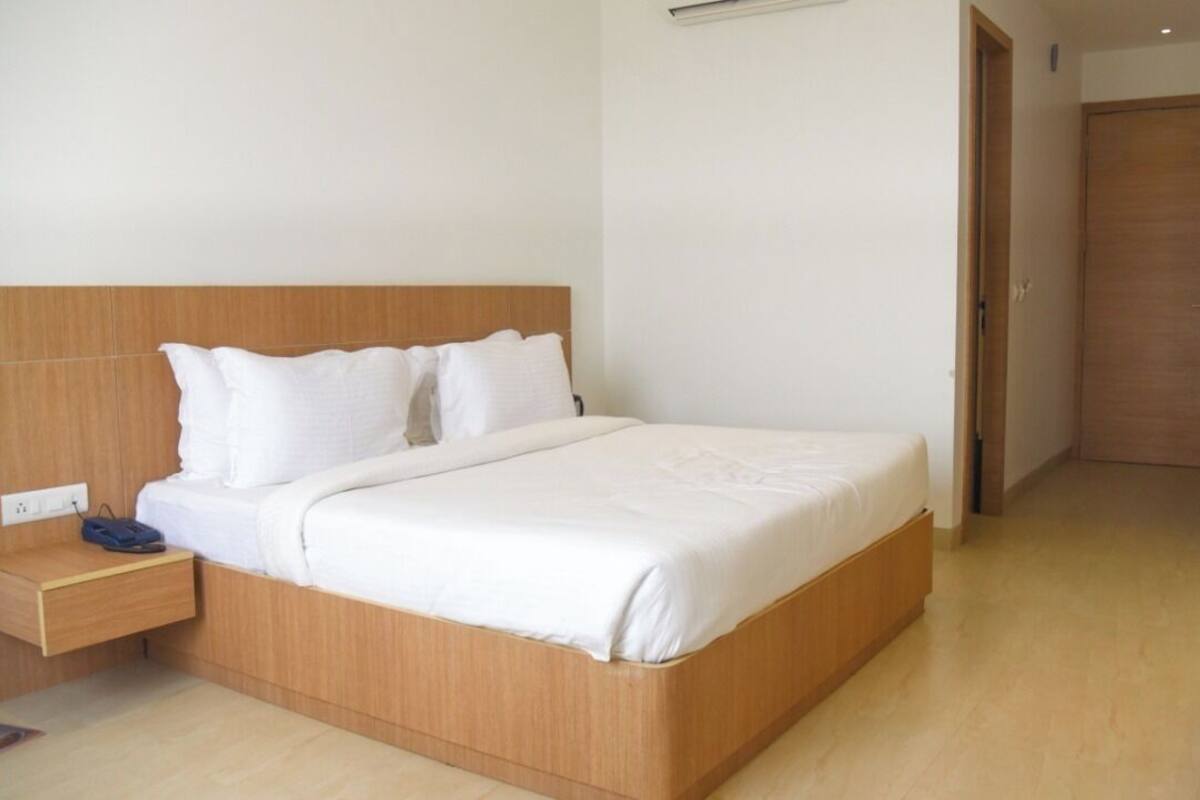 A neatly made bed with white linens, a wooden headboard, and a nightstand with a lamp.