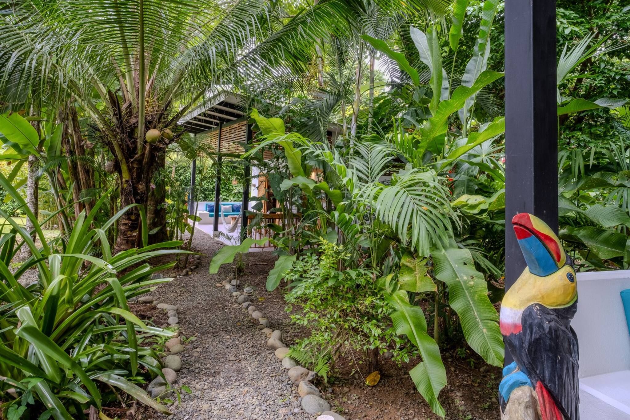 A tropical garden pathway with a hammock and a wooden structure in the background.