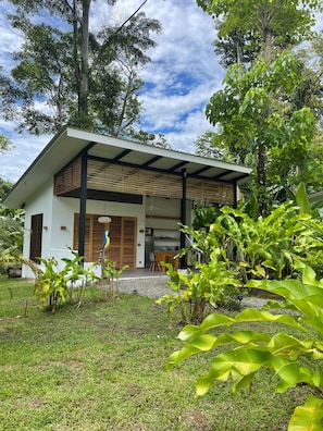 Een modern huis met een overdekte veranda, een eethoek en weelderige begroeiing.