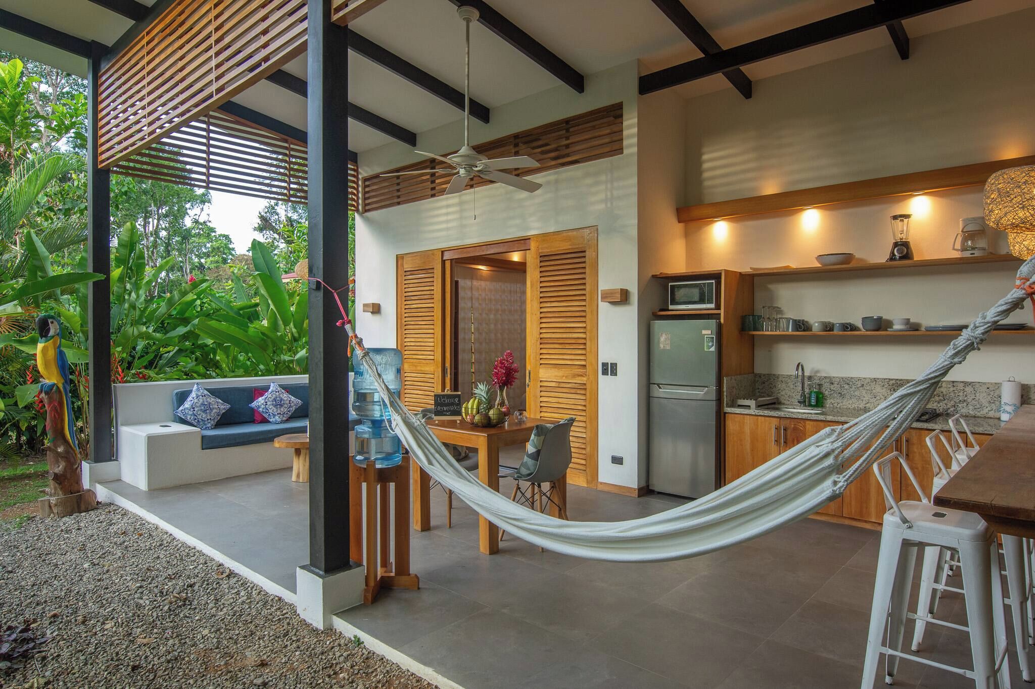 A modern outdoor kitchen with a hammock, a dining area, and a view of lush greenery.