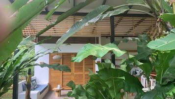 A modern house with a wooden balcony, large green leaves, and a stone wall.