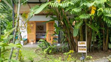 Un jardin tropical avec une maison en bois, un lit et un panneau indiquant les directions vers Lapa et Tucan.