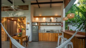 Une cuisine compacte équipée d’un réfrigérateur, d’un four à micro-ondes et de meubles en bois. Un hamac est installé dans l’espace repas, et on y trouve des tabourets de bar et une table agrémentée d’une plante.