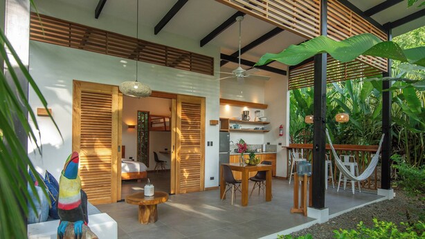 Un área de comedor exterior moderna con mesa y sillas, una hamaca y un jardín tropical.
