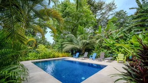 Piscina rectangular rodeada de exuberante vegetación y diversas opciones de asientos.