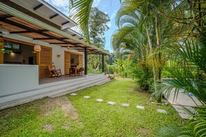 Ein modernes Haus mit überdachter Veranda, Rasen und tropischer Bepflanzung.
