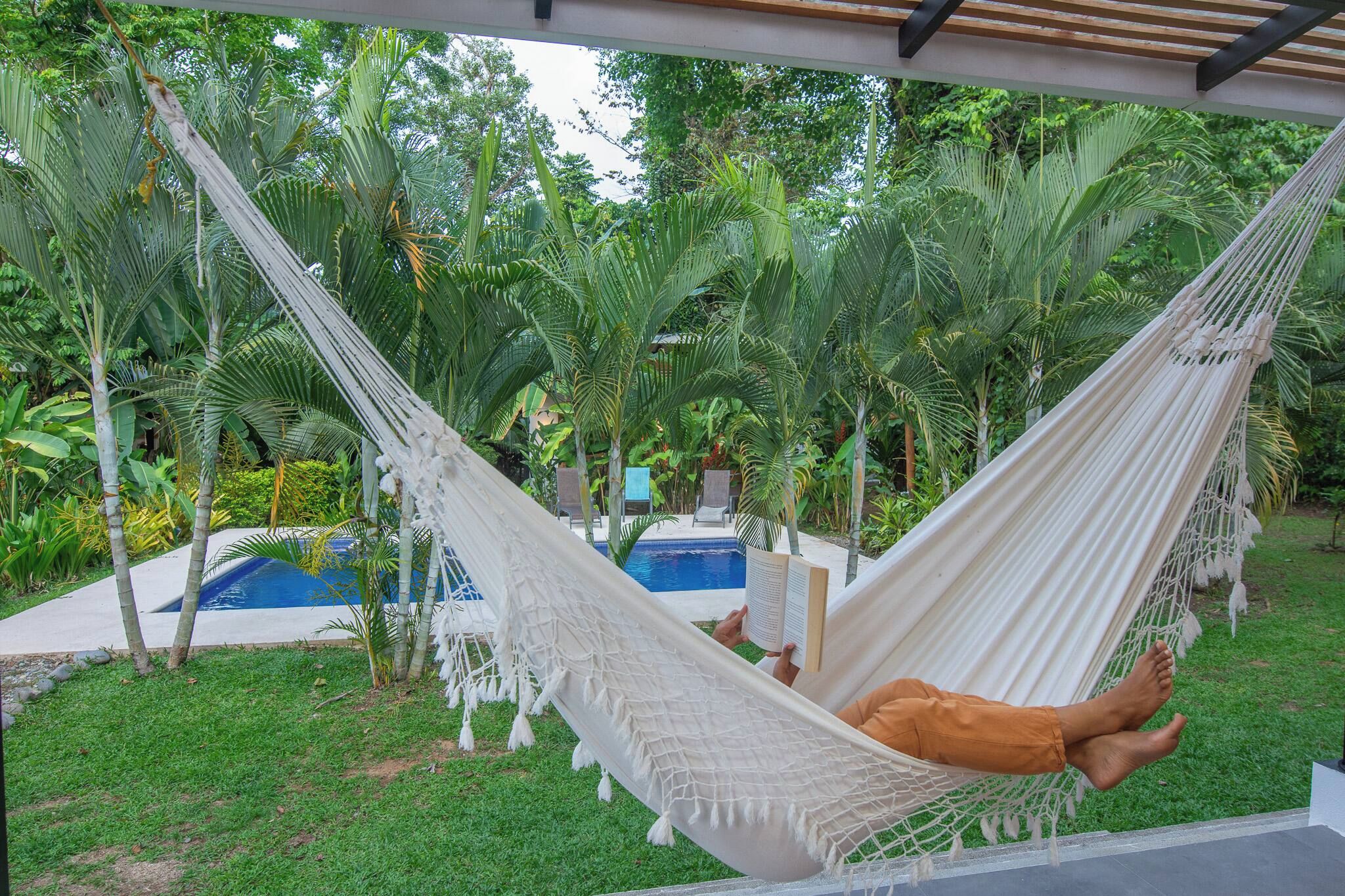 A hammock in a lush garden with a pool in the background.