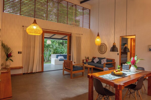 A spacious living area with a wooden dining table, two sofas, and a large window with blinds.