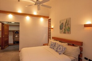 Ein Schlafzimmer mit einem Bett, einem Deckenventilator, einer Wandleuchte und einem Gemälde.