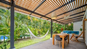 A covered patio with a dining area, a hammock, and a pool in the background.