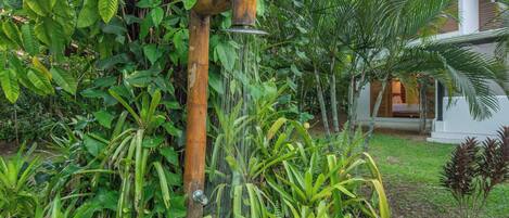 A wooden water feature with a spout, surrounded by lush greenery and a white building in the background.
