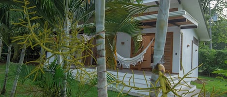Una casa moderna con una hamaca en el porche, rodeada de vegetación tropical.