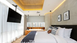 Ein modernes Hotelzimmer mit einem großen Bett, einem flachbildfernseher an der Wand, einem großen Fenster mit durchsichtigen Vorhängen und Blick auf die Stadtlandschaft.