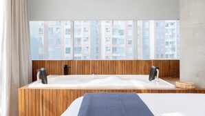 Ein modernes Badezimmer mit einem Holzbadezimmerwaschtisch, einer großzügigen Badewanne und Blick auf eine Stadtlandschaft durch ein großes Fenster.