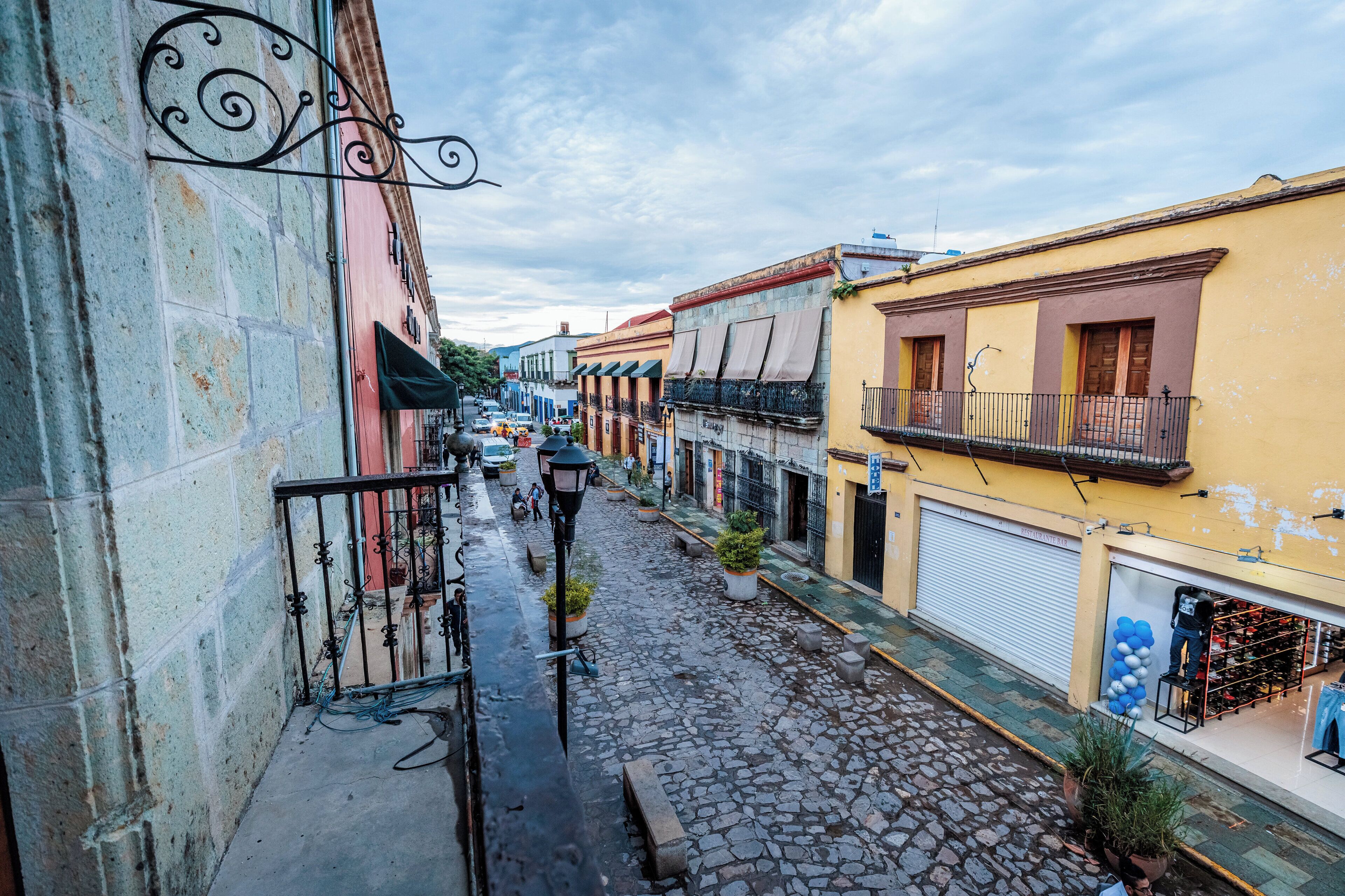 A cobblestone street with buildings on either side, featuring balconies and storefronts.