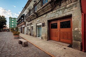 A cobblestone street with a row of buildings, including a green multi-story building and a stone building with a large wooden door. - Casa 1800 Oaxaca Boutique Hotel (Oaxaca)