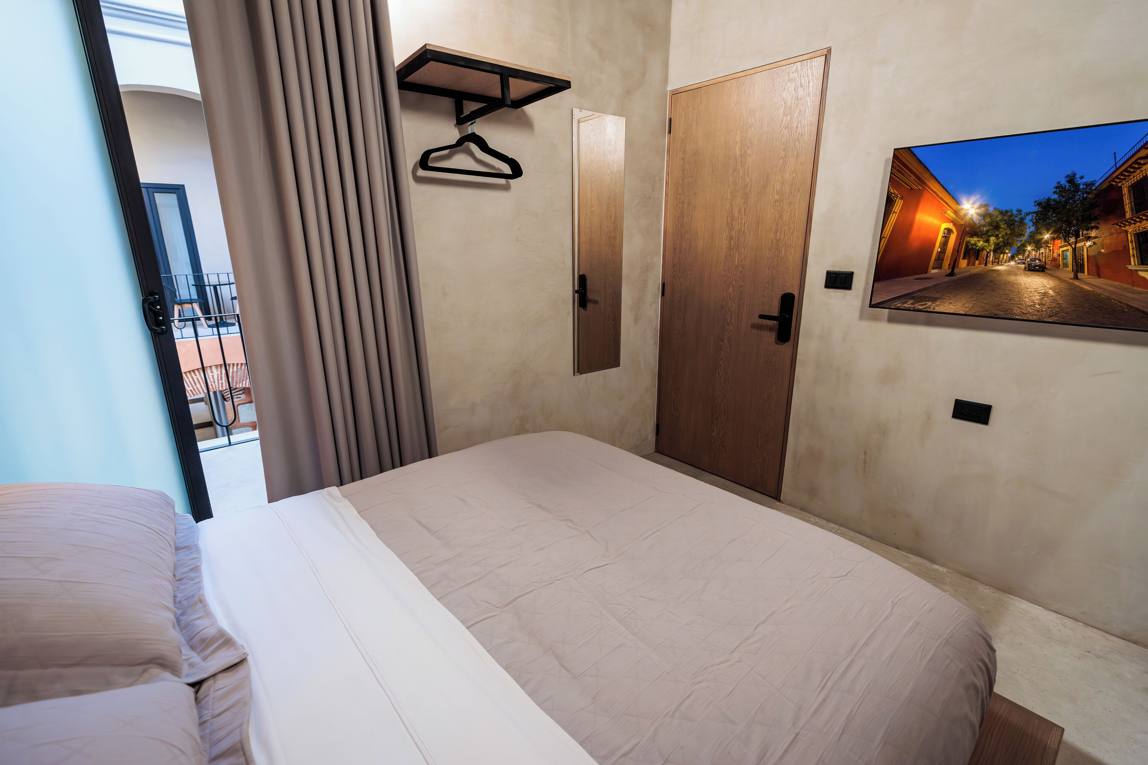 A hotel room with a bed, a wooden door, a coat rack, and a framed photo on the wall.