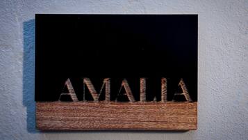 Un letrero de madera con el nombre "AMALIA" sujeto a una pared con textura.