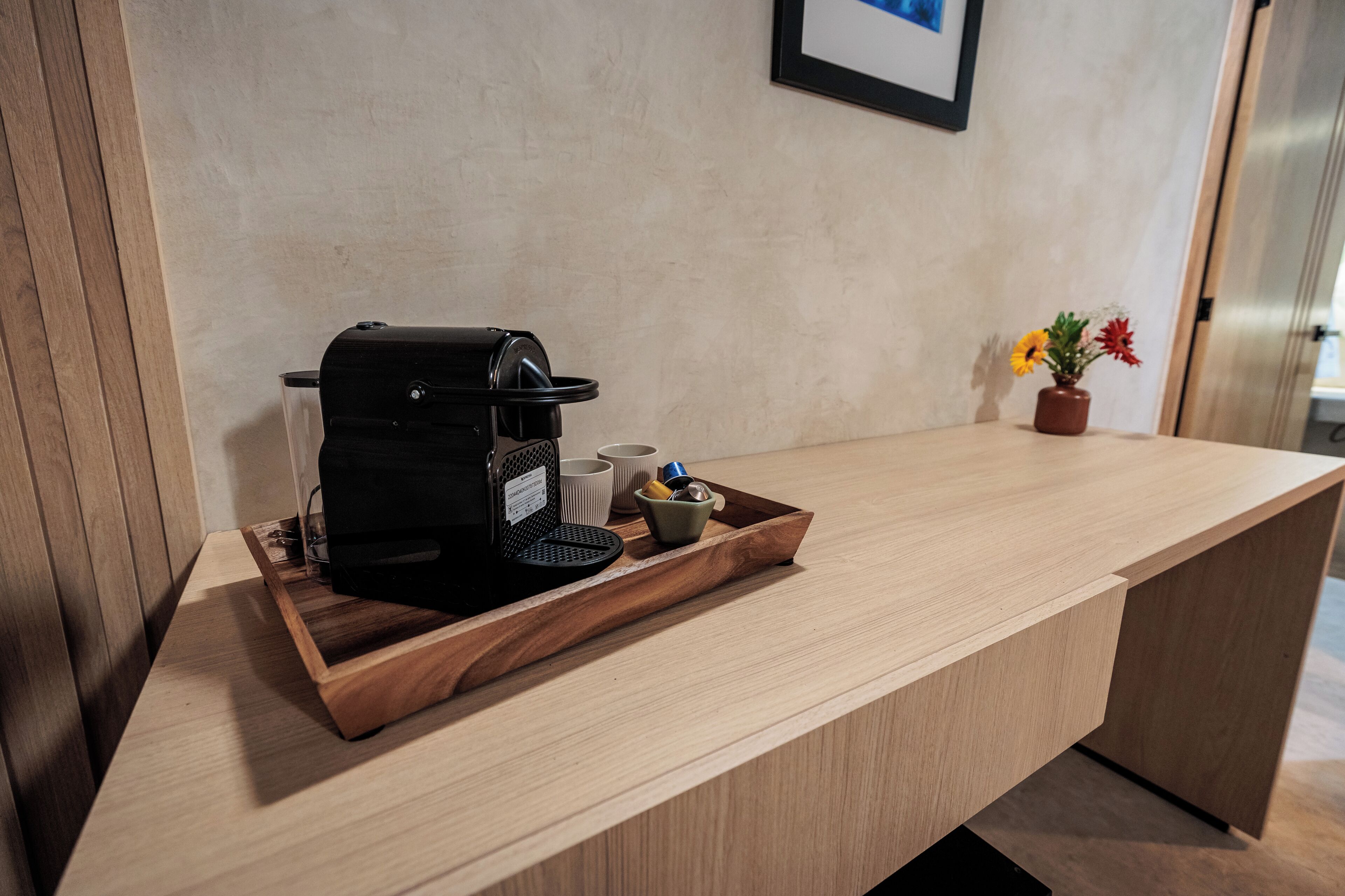 Un comptoir d’accueil en bois, avec une machine à café, un plateau contenant des tasses et un petit bol, ainsi qu’un vase avec des fleurs.