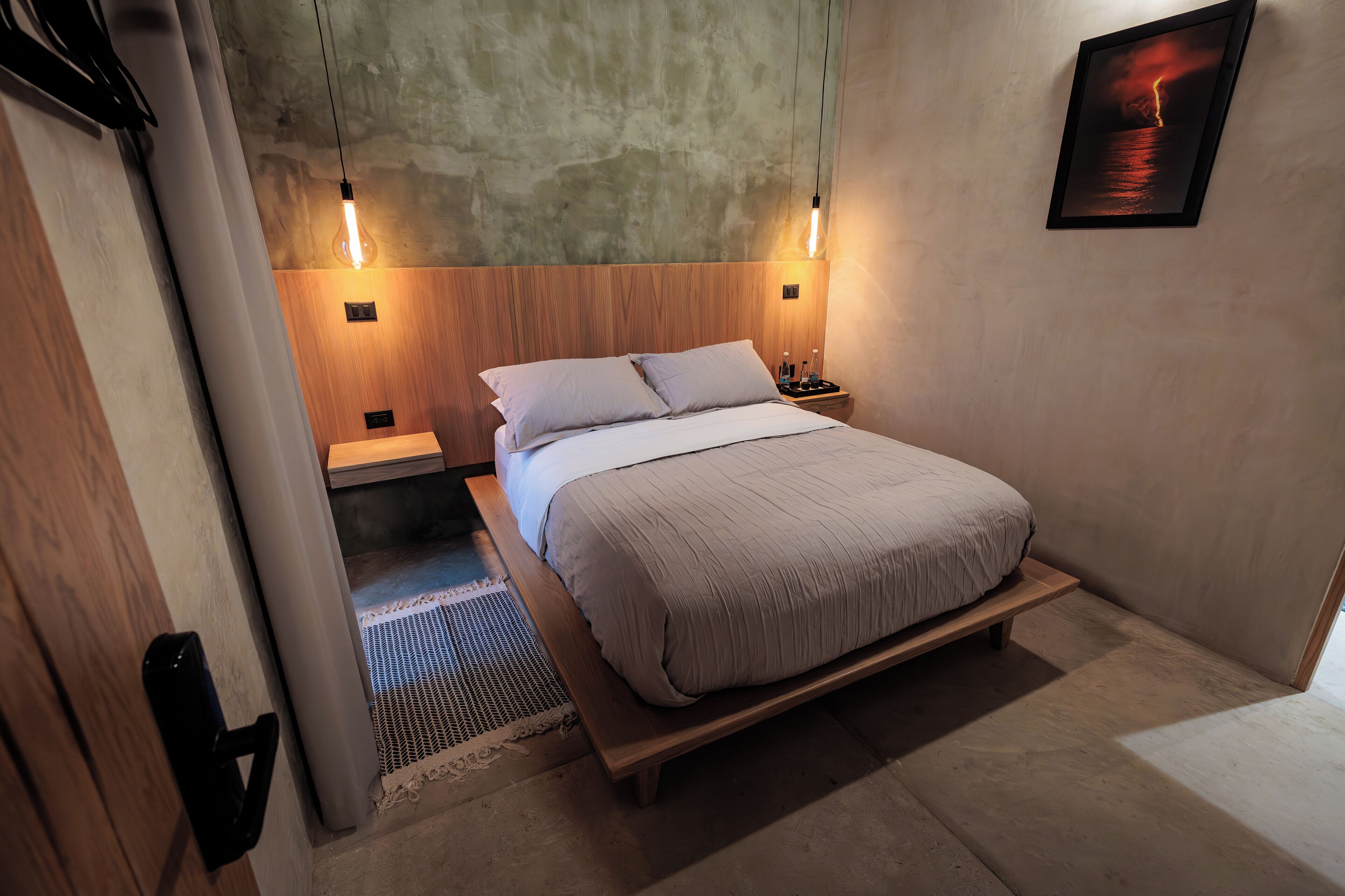 A bedroom with a wooden bed, two bedside tables, a wall-mounted light fixture, and a framed picture.