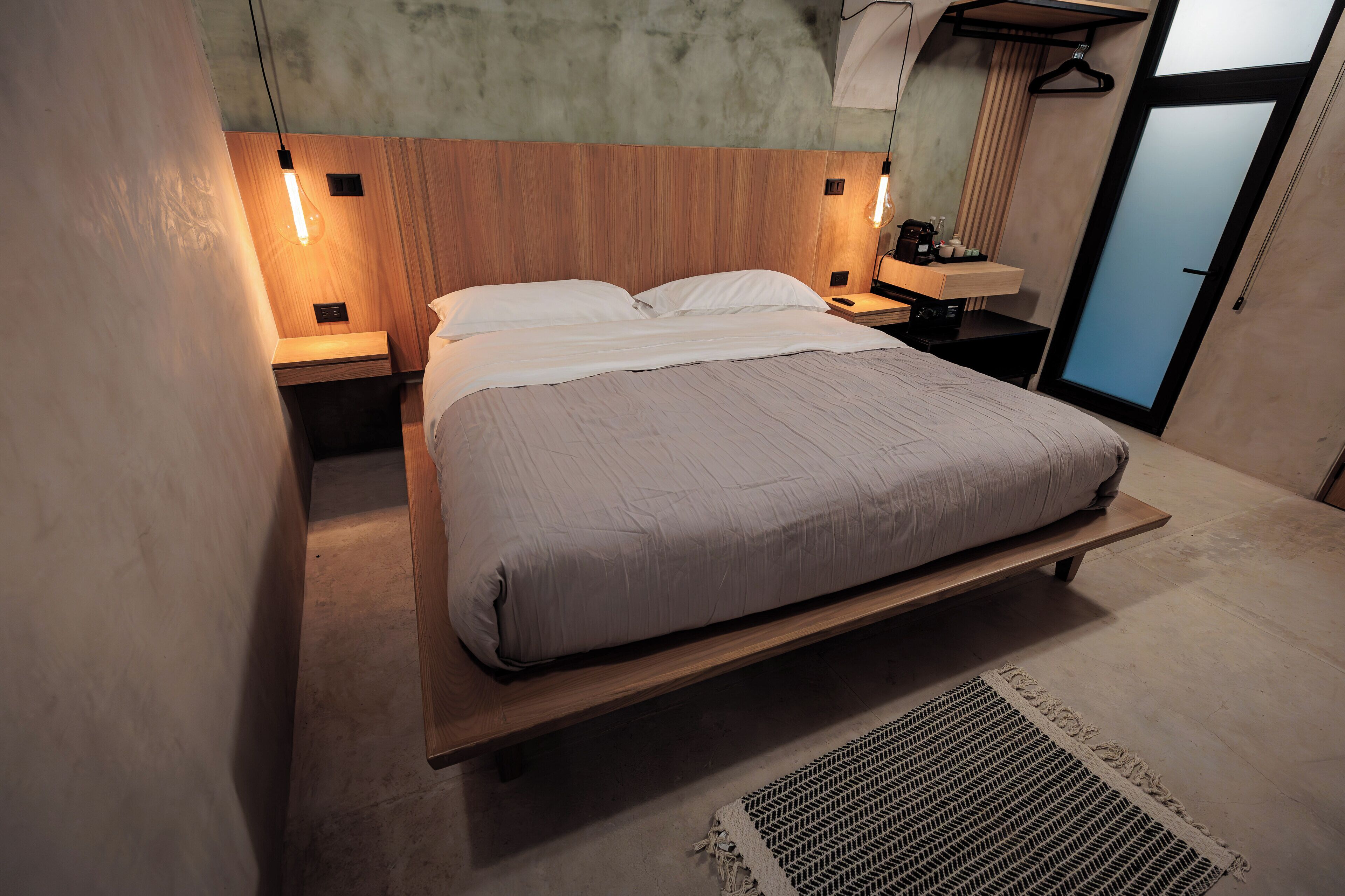 A modern bedroom with a wooden headboard, a single bed, bedside tables with lamps, and a hanging light fixture.
