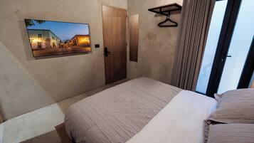 Ein Schlafzimmer mit einem Bett, einer Tür, einem Kleiderständer und einem an der Wand befestigten Fernseher, der eine Straßenszene zeigt.