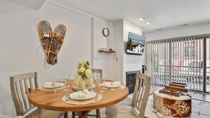 A dining area with a round wooden table set for four, surrounded by chairs. A clock and a television are mounted on the wall. - New Claim by Park City Vacations (Park City)