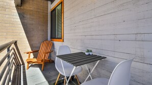A wooden deck with a table and chairs, a window with shutters, and a brick wall. - New Claim by Park City Vacations (Park City)