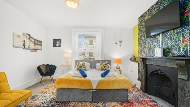 Ein modernes Schlafzimmer mit einem Bett, einem gelben Sessel, einem Kamin und Kunstwerken an den Wänden.