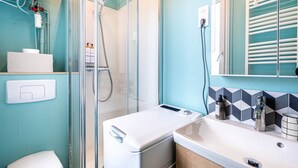 A bathroom with a glass-enclosed shower, a white toilet, a washing machine, and a sink with a mirror above it.