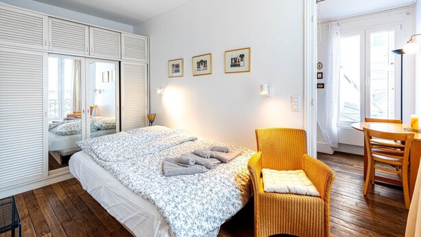 A bedroom with a bed, a chair, a table, and a wardrobe.