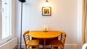 A round wooden table with four chairs, a lit floor lamp, and a framed picture on the wall.
