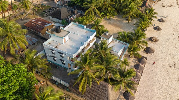 An aerial view of a beachfront hotel with multiple buildings, including a prominent multi-story structure with balconies and a smaller adjacent building. - Sands inn Hotel (Pwani Mchangani)
