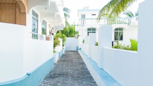 A narrow, paved alleyway between white buildings with blue trim, leading to a gated entrance. - Sands inn Hotel (Pwani Mchangani)